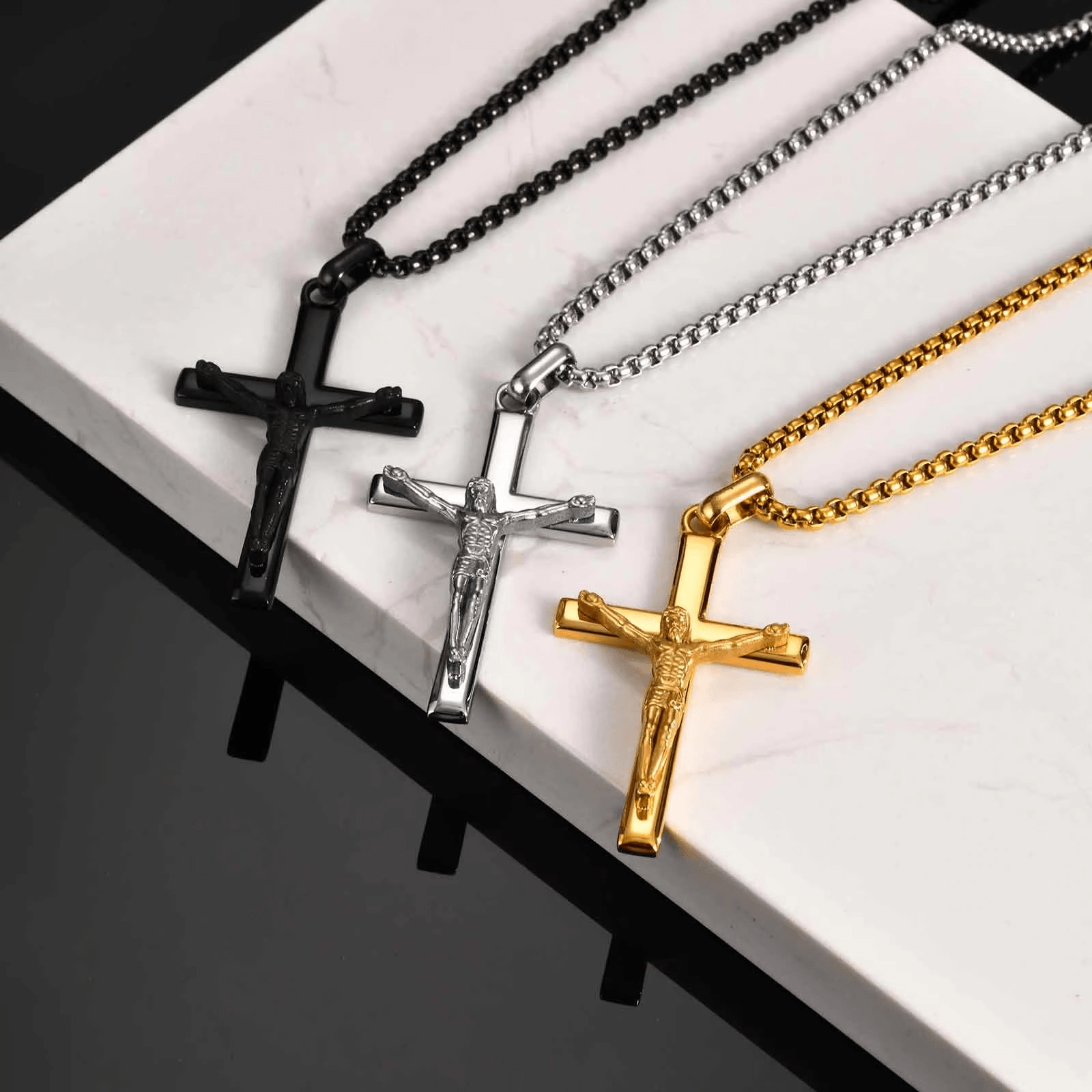 Four cross necklaces in black, silver, and gold on a white surface.