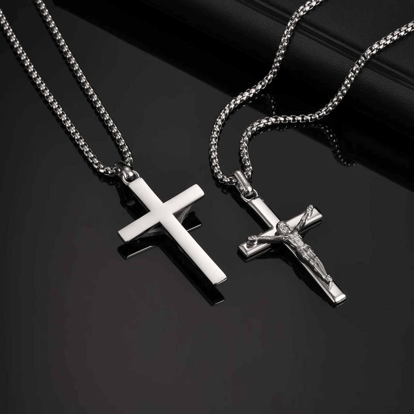 Two silver cross necklaces on a dark surface