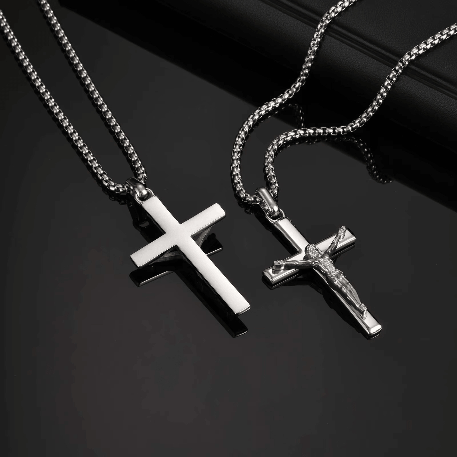 Two silver cross necklaces on a dark surface