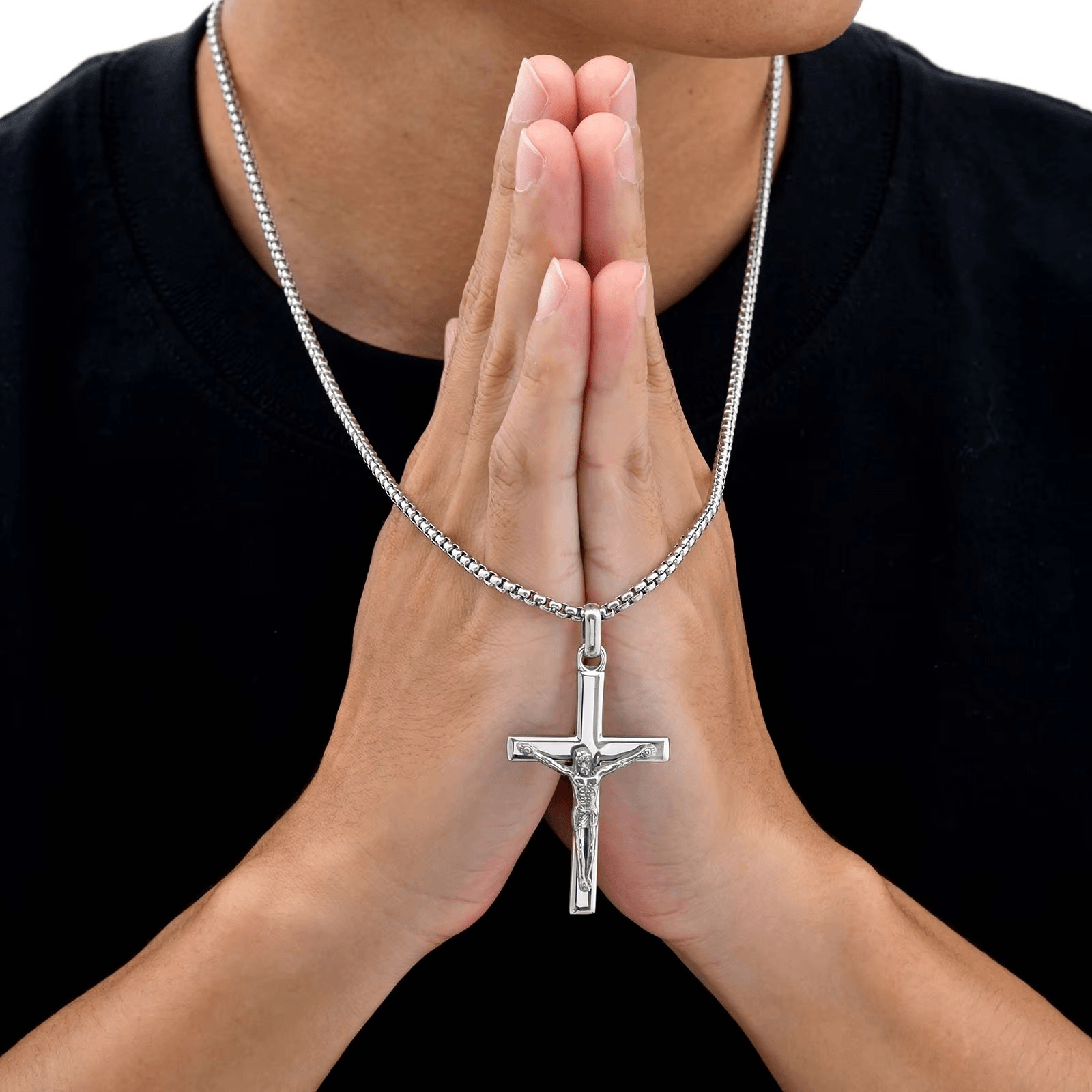 Person wearing a silver necklace with a cross pendant, hands clasped together.