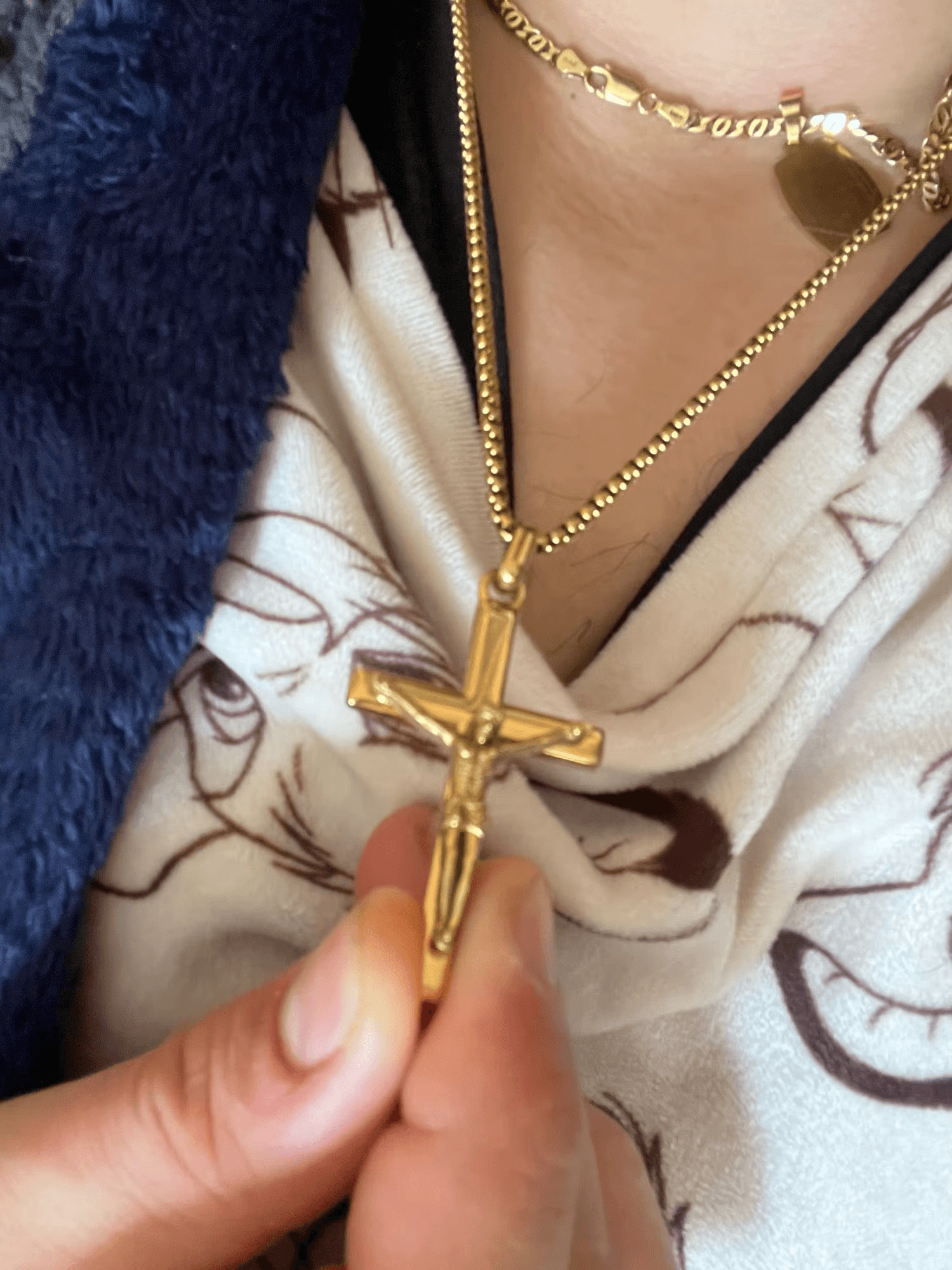 Gold cross pendant held by a hand with a patterned fabric background