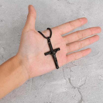 Hand holding a black cross necklace against a gray concrete background