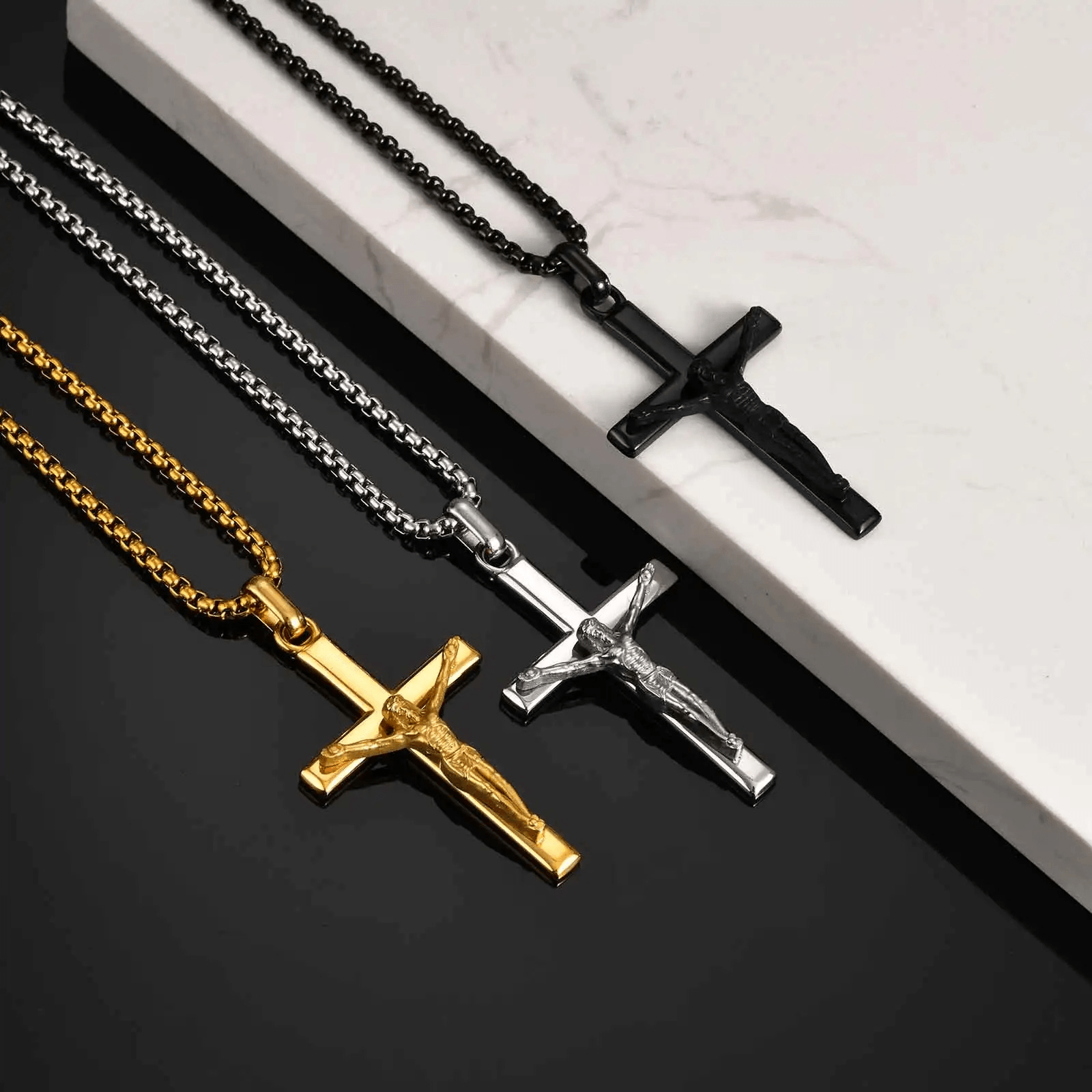 Four cross necklaces in gold, silver, and black on a reflective surface.